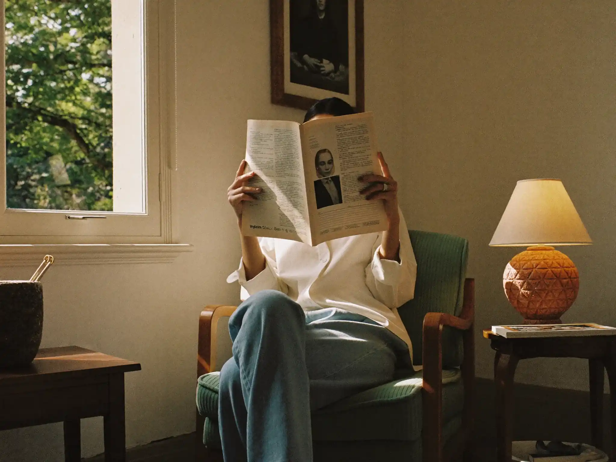 Adult reading a paper journal by a sunny window with a cup of tea